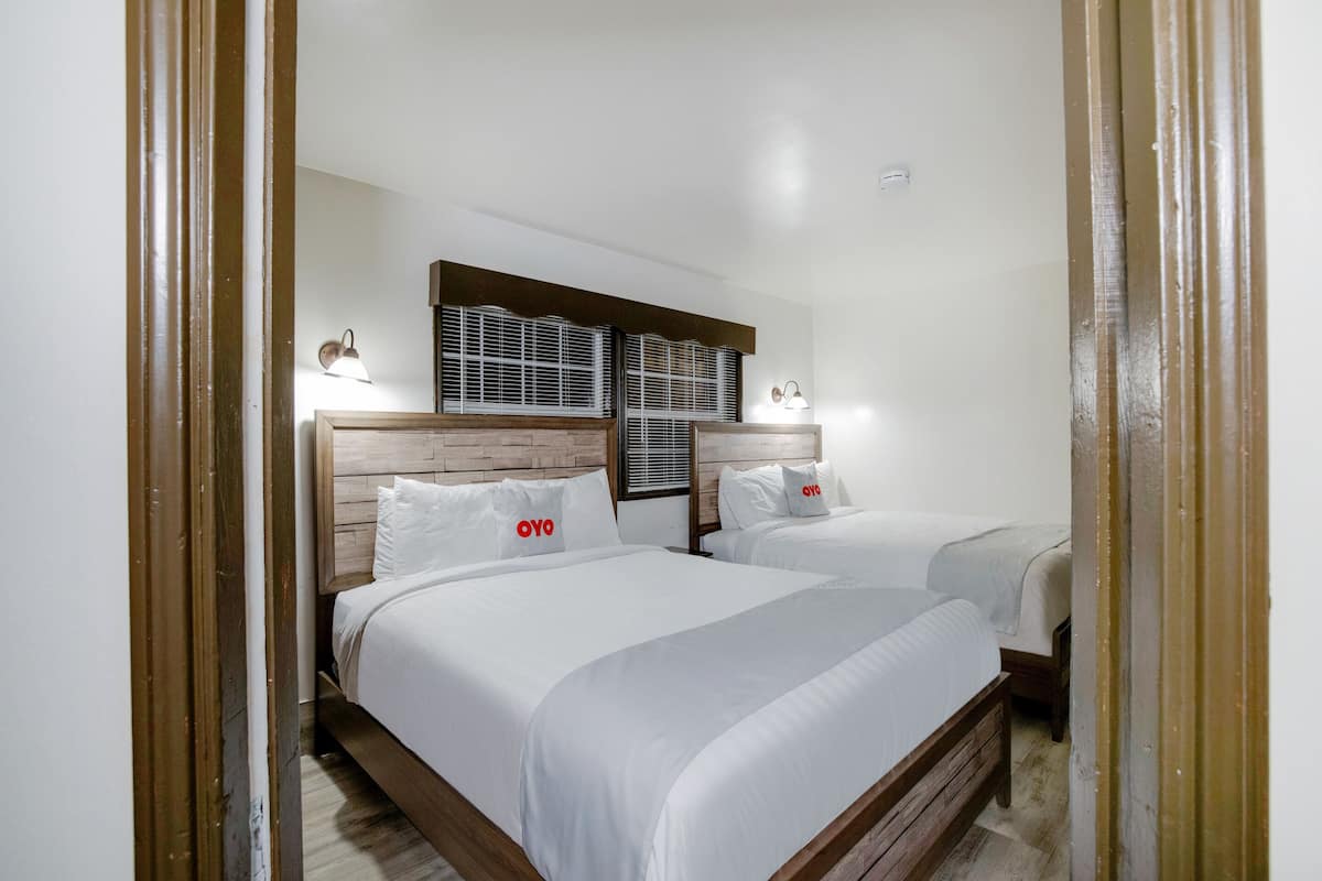 Une chambre d’hôtel avec deux lits, des têtes de lit en bois, du linge de lit blanc et des lampes fixées au mur.