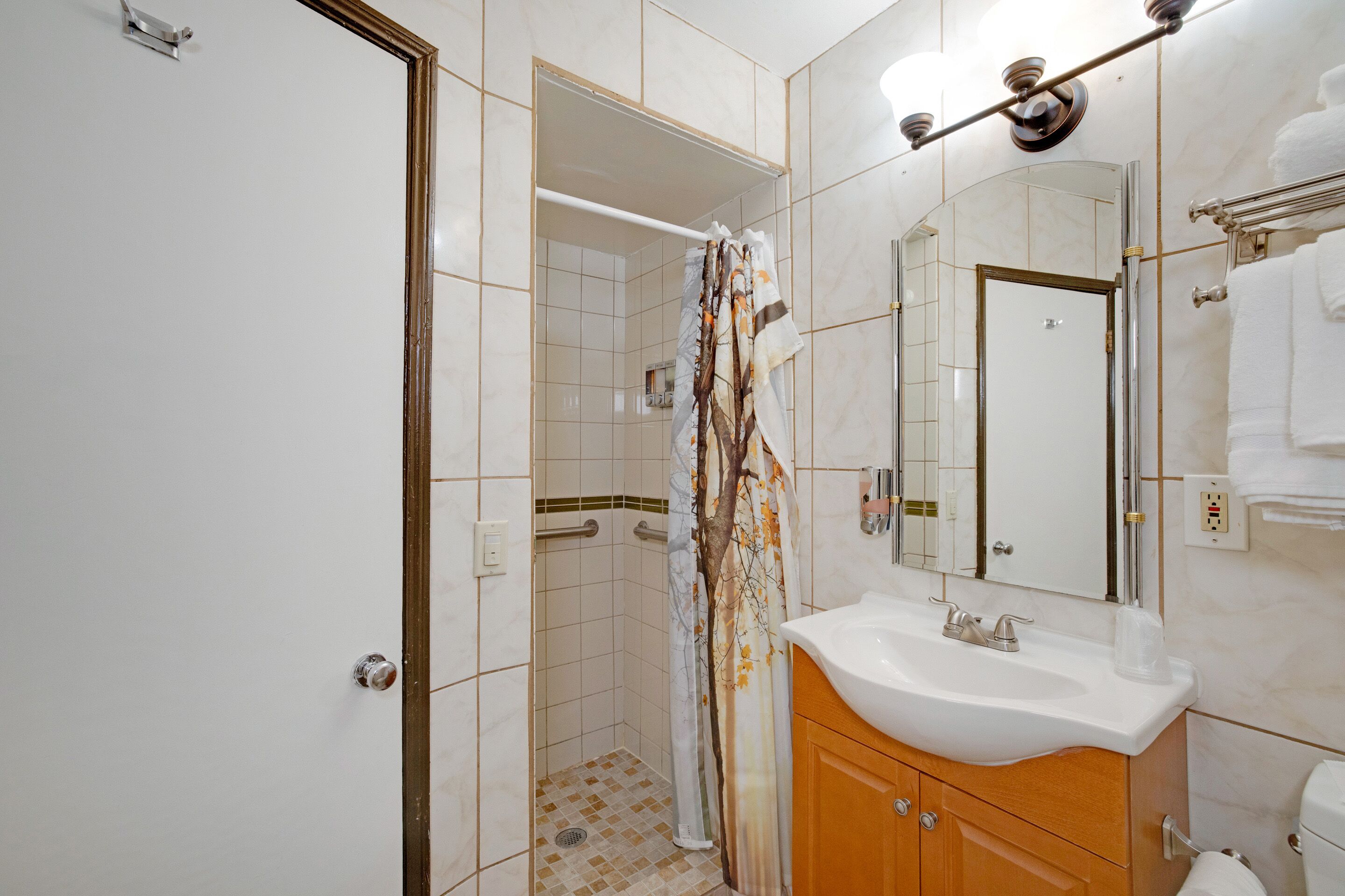 A bathroom with a shower, a sink, a mirror, and a toilet.
