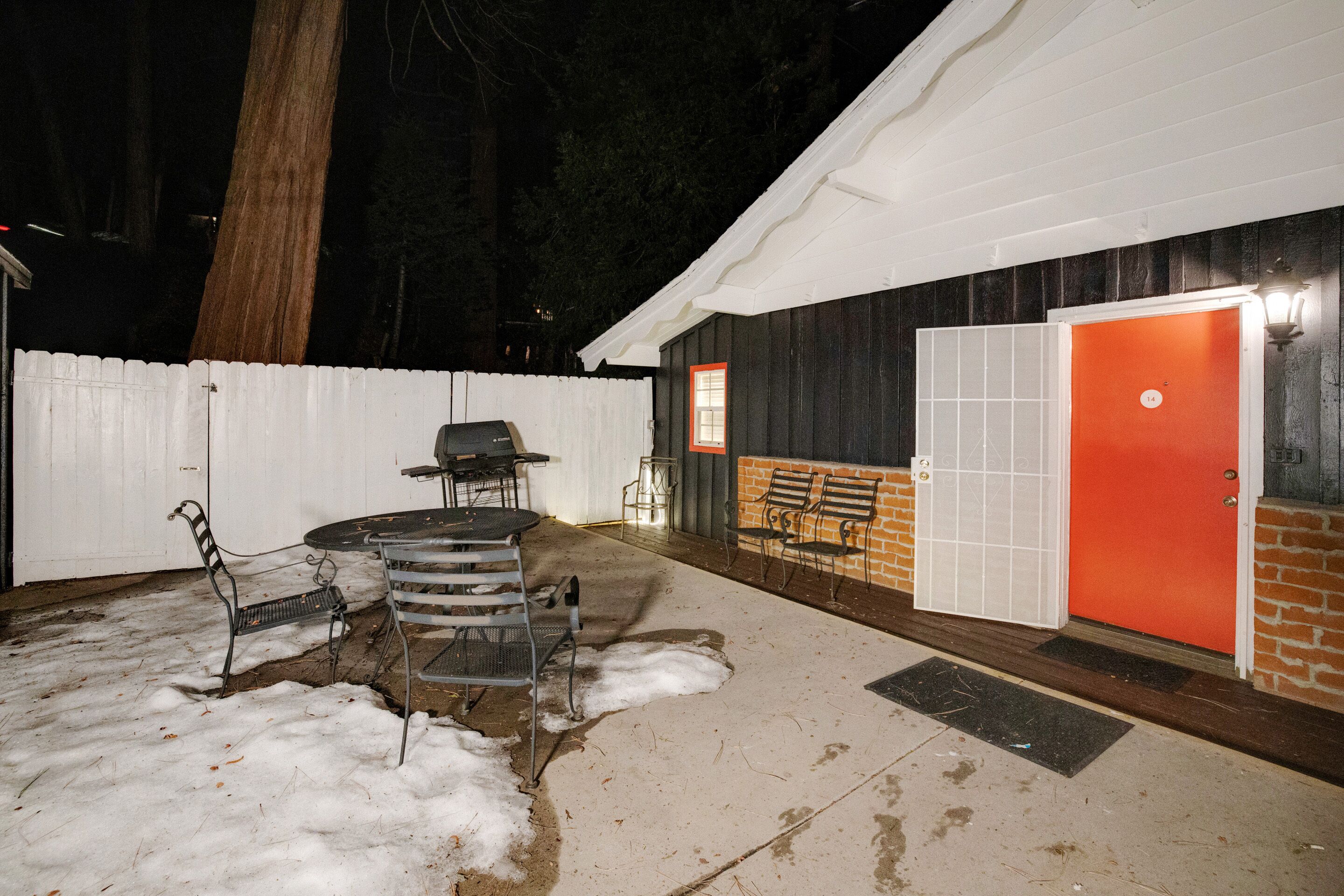 A patio with a table and chairs, a barbecue grill, and a red door.