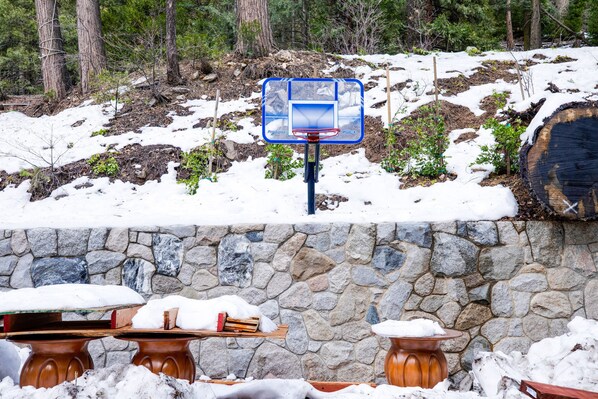 A snow-covered outdoor area with a stone wall and wooden tables. - Arrowhead Tree Top Lodge (Lake Arrowhead)