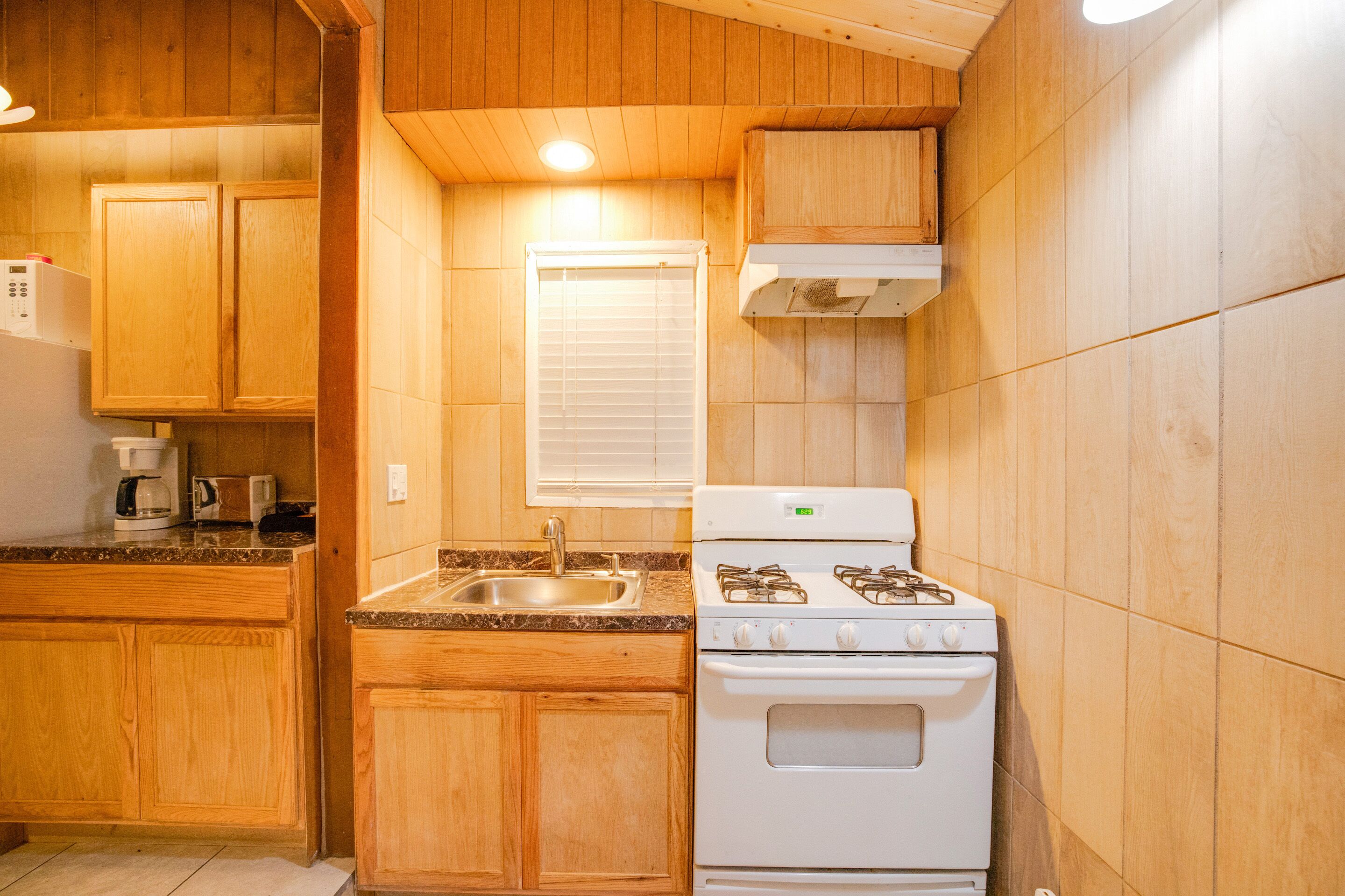 Una cocina con armarios de madera, una estufa blanca, un fregadero y una ventana con persianas.