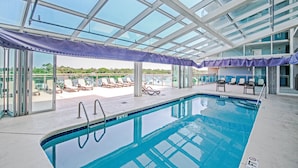A swimming pool with clear blue water, surrounded by lounge chairs and a glass ceiling.