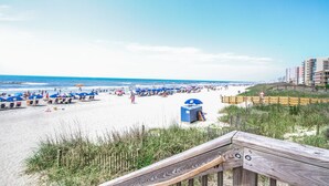 A beach with a wooden boardwalk leading to the shore, featuring a blue lifeguard station and beach umbrellas.