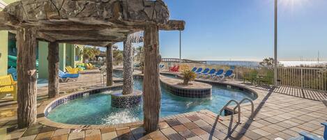 A pool area with a stone arch, lounge chairs, and a view of the sea.
