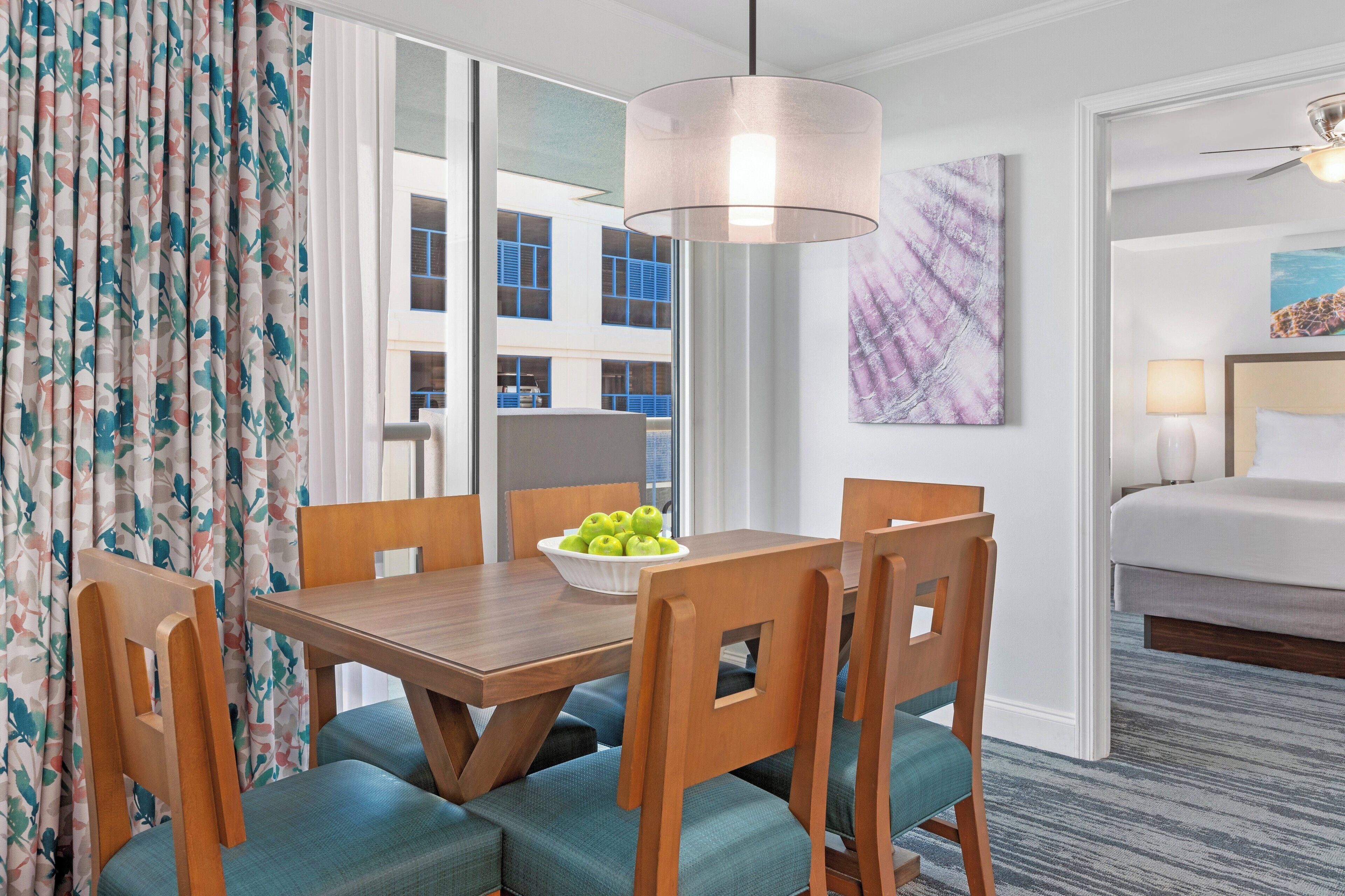 A hotel room with a dining area featuring wooden furniture and a bowl of green apples.