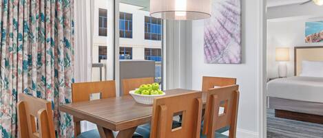 A hotel room with a dining area featuring wooden furniture and a bowl of green apples.