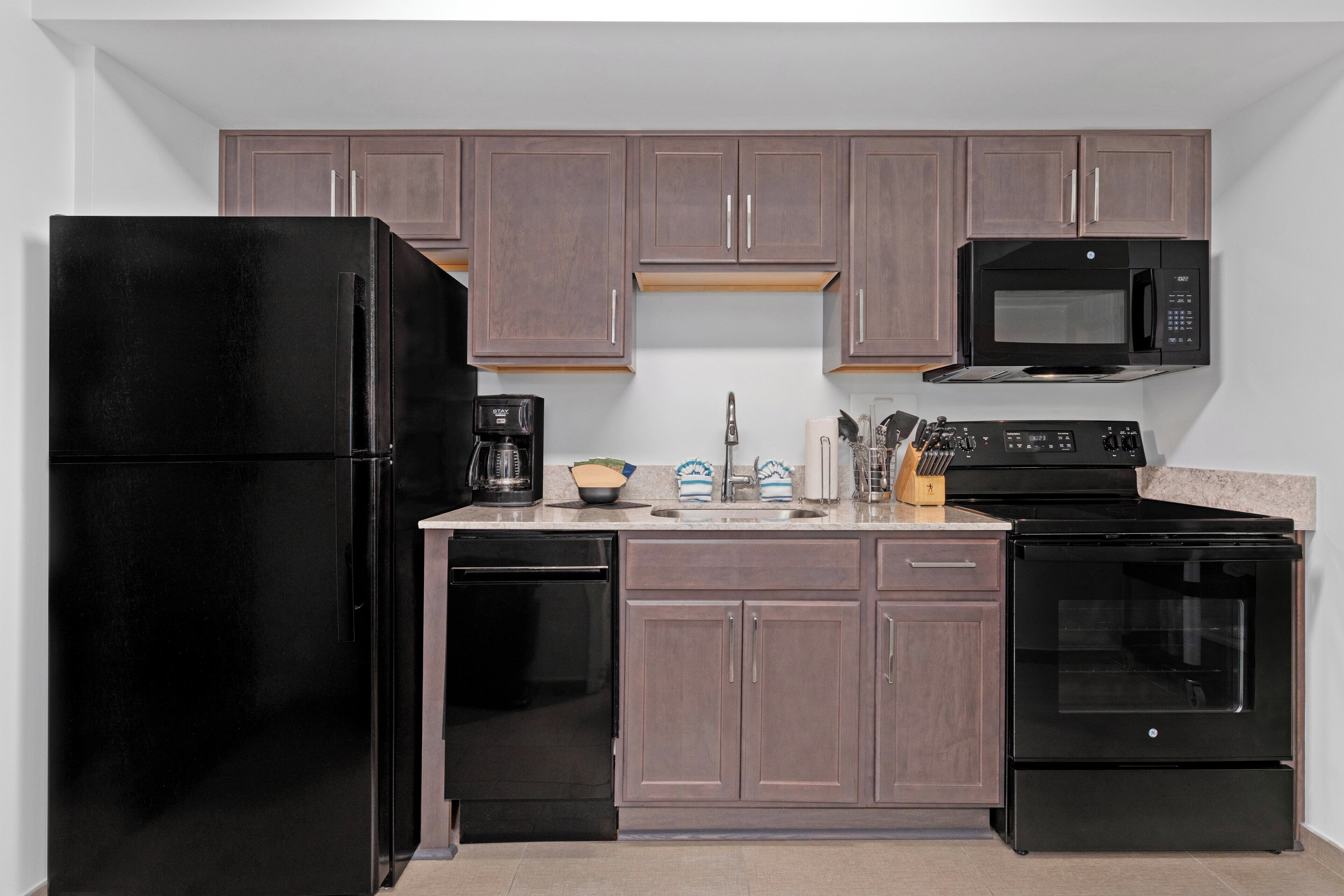 A kitchen with dark cabinets, a black refrigerator, a microwave, a coffee maker, and a dishwasher.