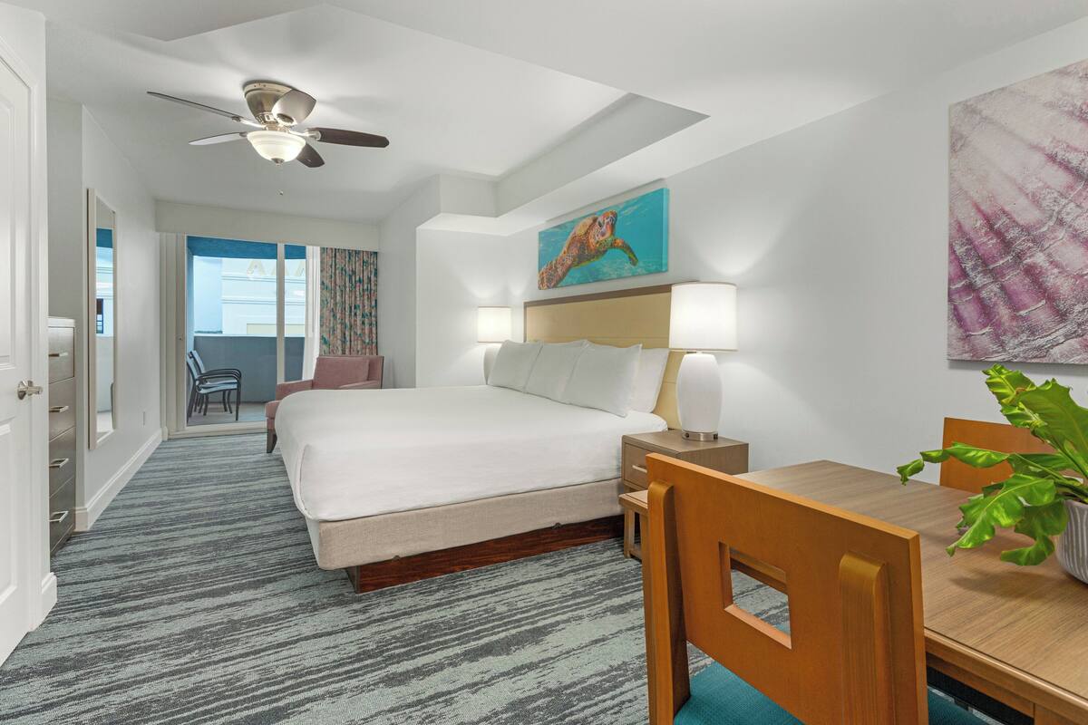 A hotel room with a bed, bedside table, lamp, and a dining table with chairs.