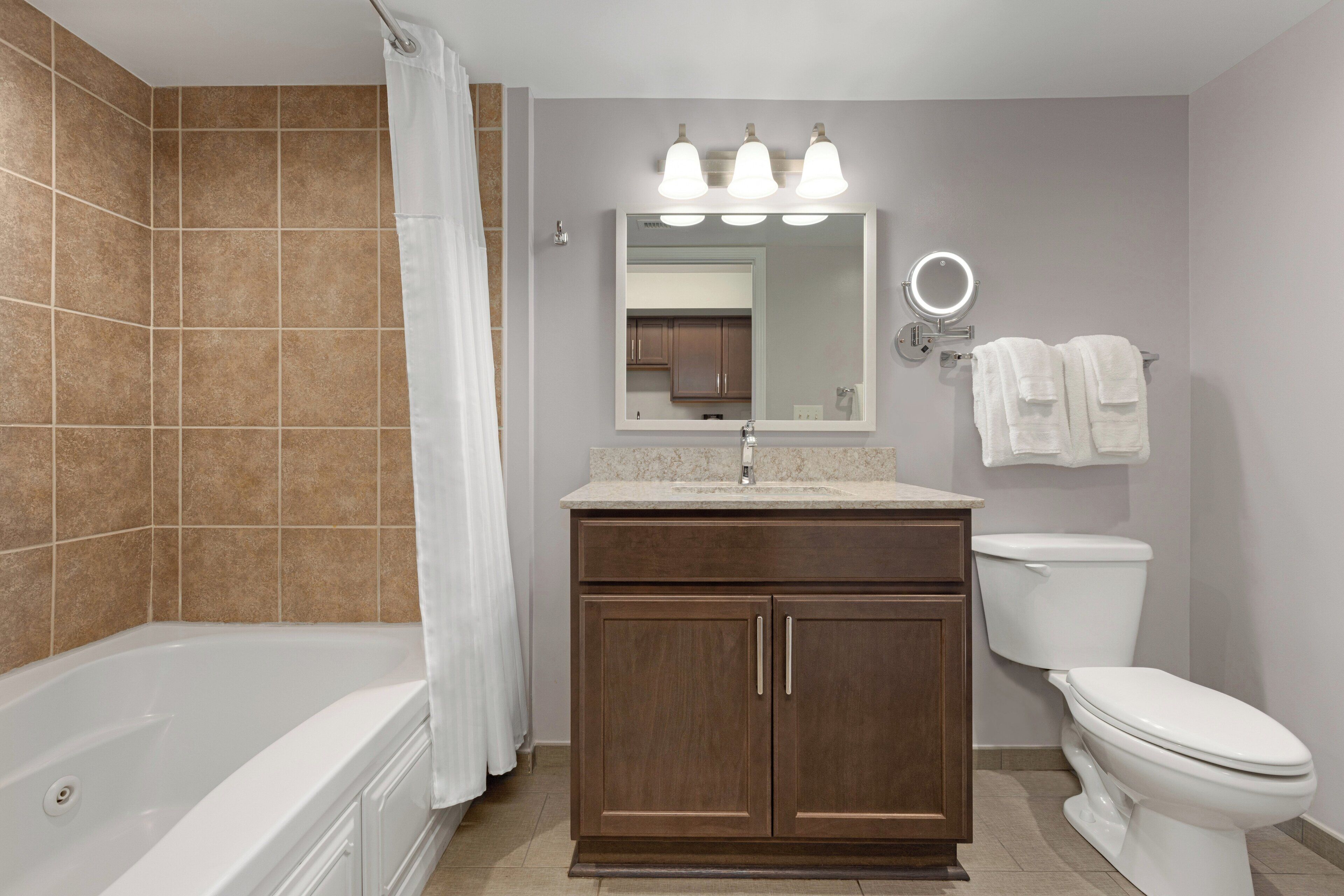 A bathroom with a bathtub, vanity, toilet, and a mirror with lights.