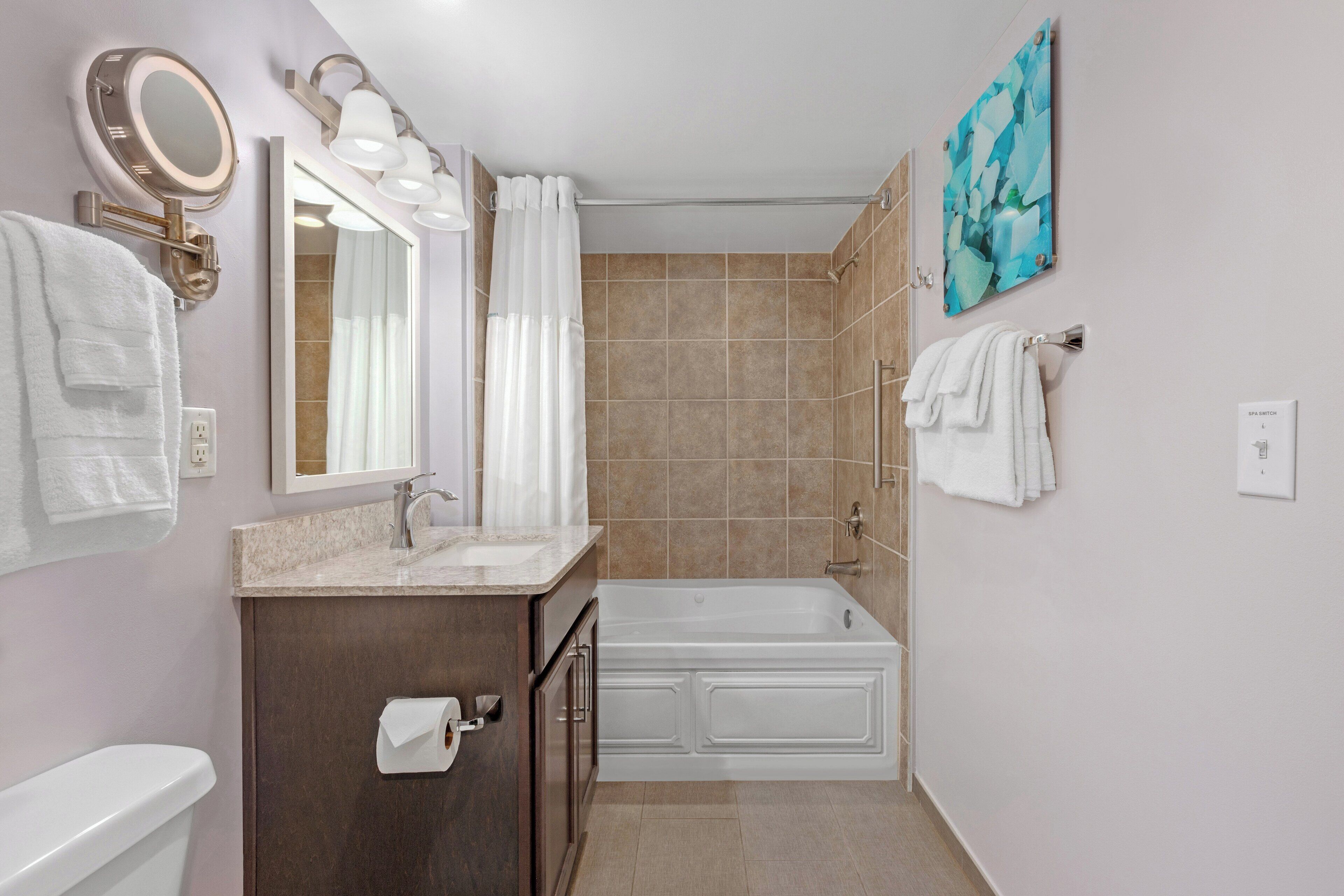A bathroom with a toilet, sink, and bathtub. There are towels hanging on the wall and a painting above the bathtub.