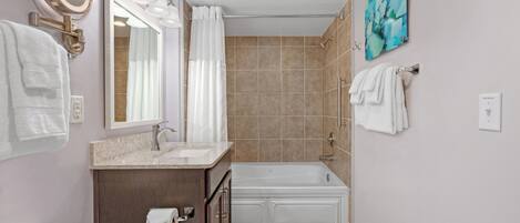 A bathroom with a toilet, sink, and bathtub. There are towels hanging on the wall and a painting above the bathtub.