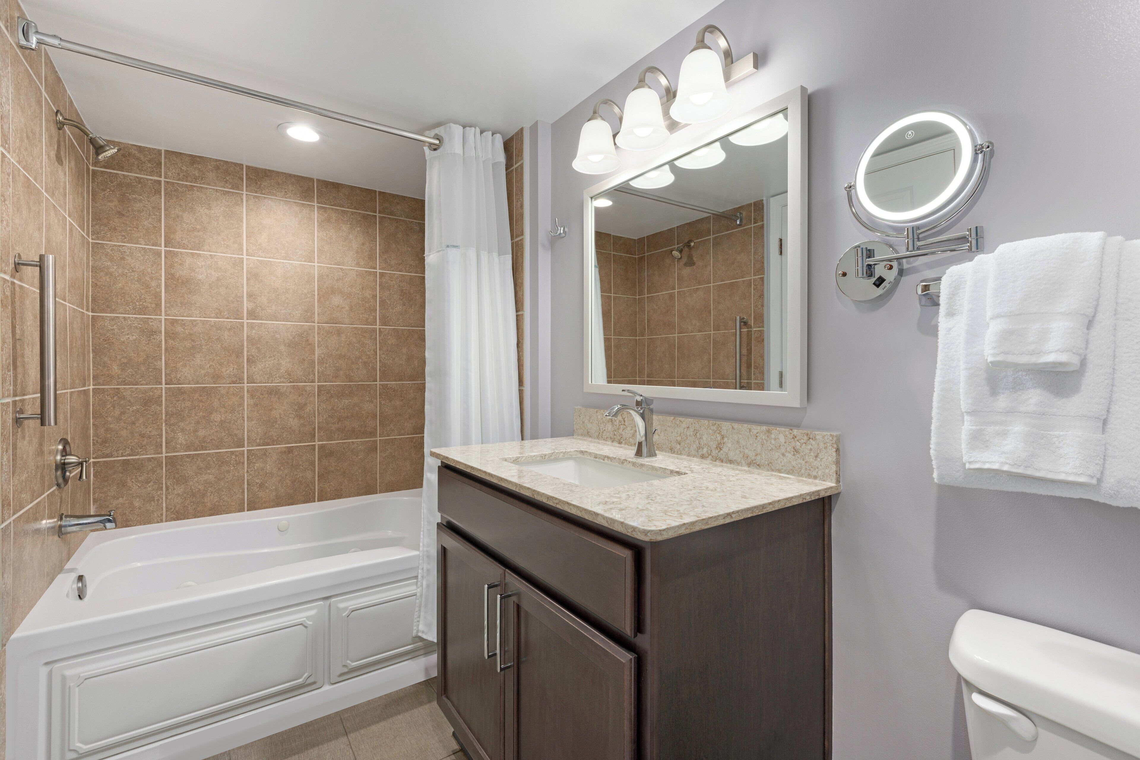 A modern bathroom with a bathtub, vanity, and a large mirror with lights.