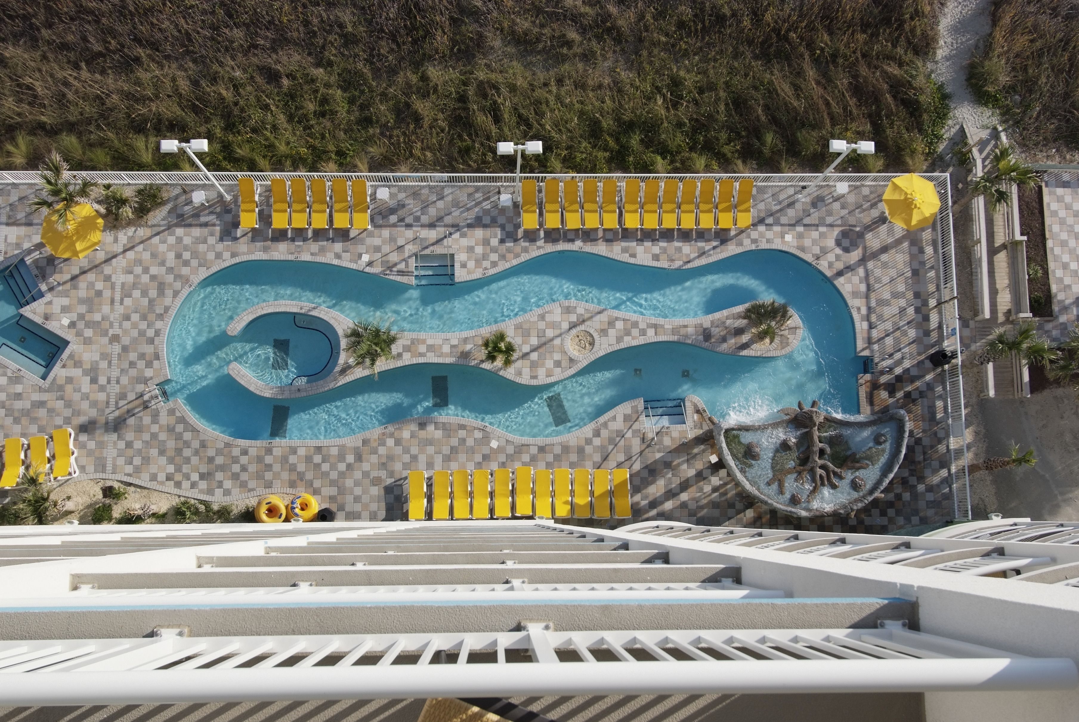 An aerial view of a swimming pool with a wavy design, surrounded by sun loungers and umbrellas.