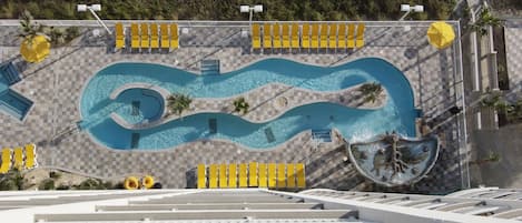An aerial view of a swimming pool with a wavy design, surrounded by sun loungers and umbrellas.