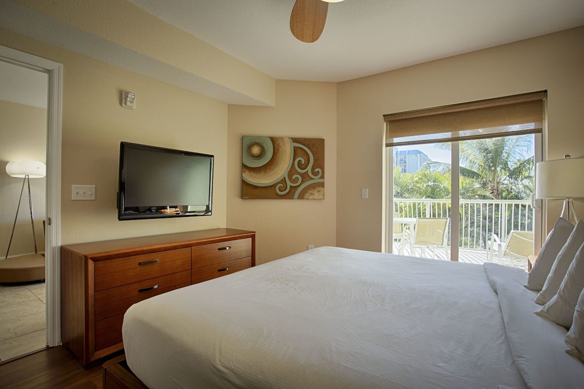 Een hotelkamer met een bed, een televisie, een houten dressoir, een schilderij en een balkon met tuinmeubilair.