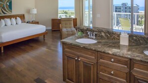 A bedroom with a large bed, a nightstand, a chair, and a view of the ocean.