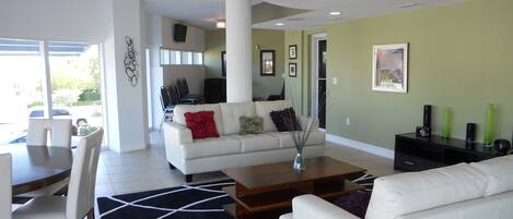 A modern living room with a white sofa, a coffee table, and a dining area with chairs and a table.