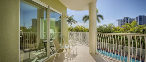 A balcony with a glass door, outdoor seating, and a pool view.