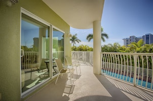 A balcony with a glass door, outdoor seating, and a pool view.