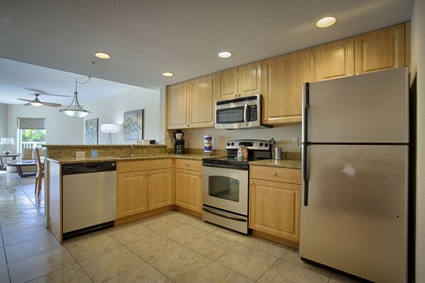 A modern kitchen with wooden cabinets, stainless steel appliances, and a tiled floor. - Crystal Palms Beach Resort (Treasure Island)