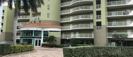 Un hotel de varios pisos con balcones, una entrada principal y una palmera.