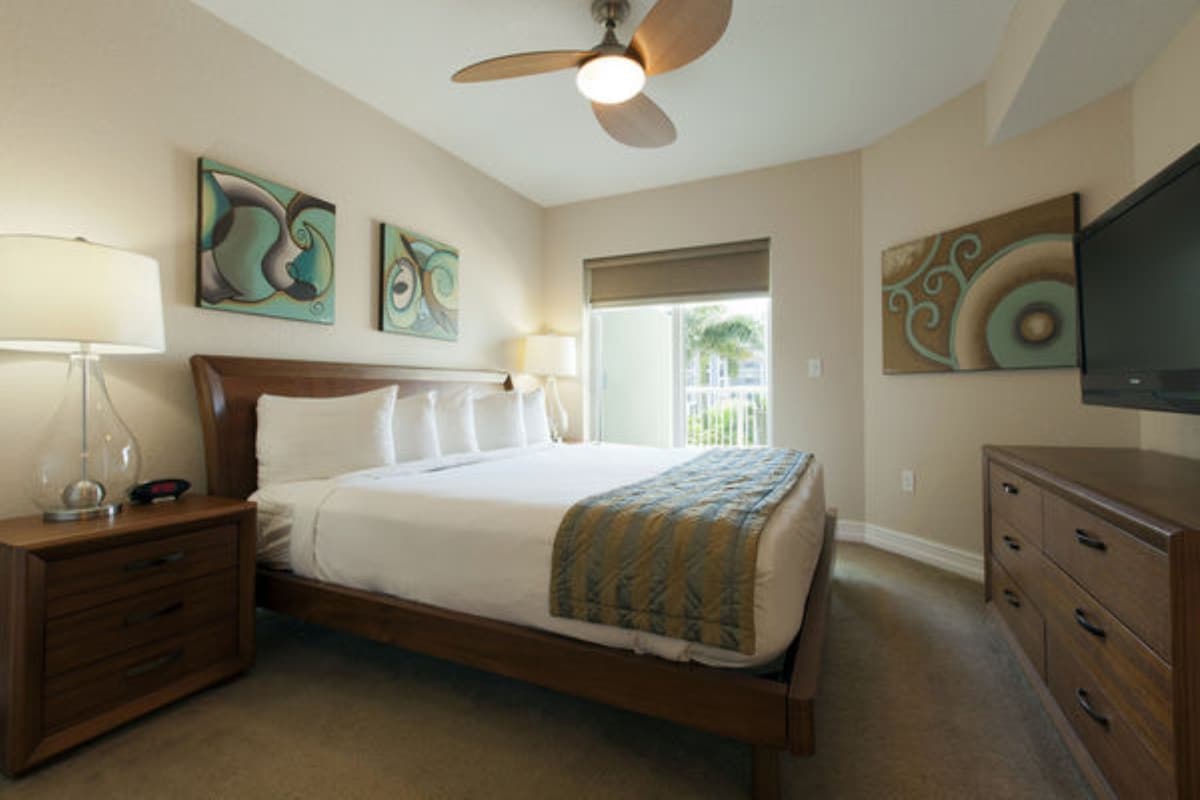 Een hotelkamer met een bed, nachtkastje, dressoir, plafondventilator en kunst aan de muur.