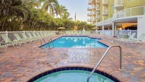 A swimming pool with a brick border, surrounded by lounge chairs and palm trees.