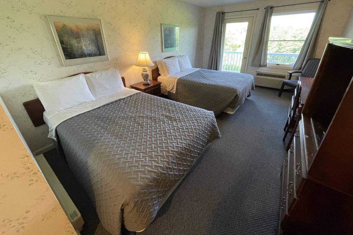 A hotel room with two beds, a desk, a chair, a TV, and a window with curtains.