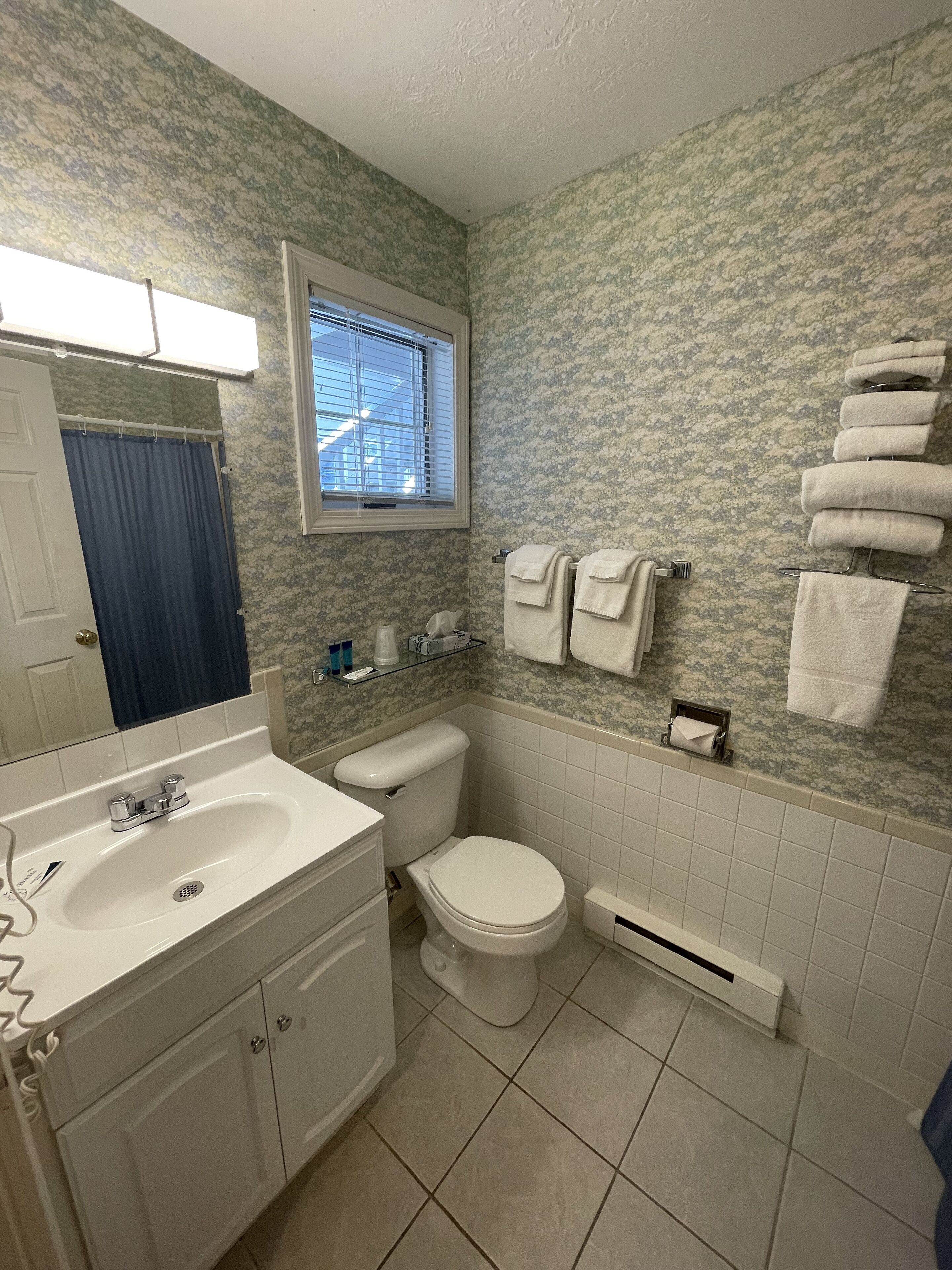A bathroom with a white sink, toilet, and bathtub. There is a window above the toilet, and towels are hung on a rack.