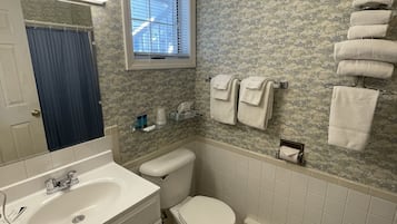 A bathroom with a white sink, toilet, and bathtub. There is a window above the toilet, and towels are hung on a rack.