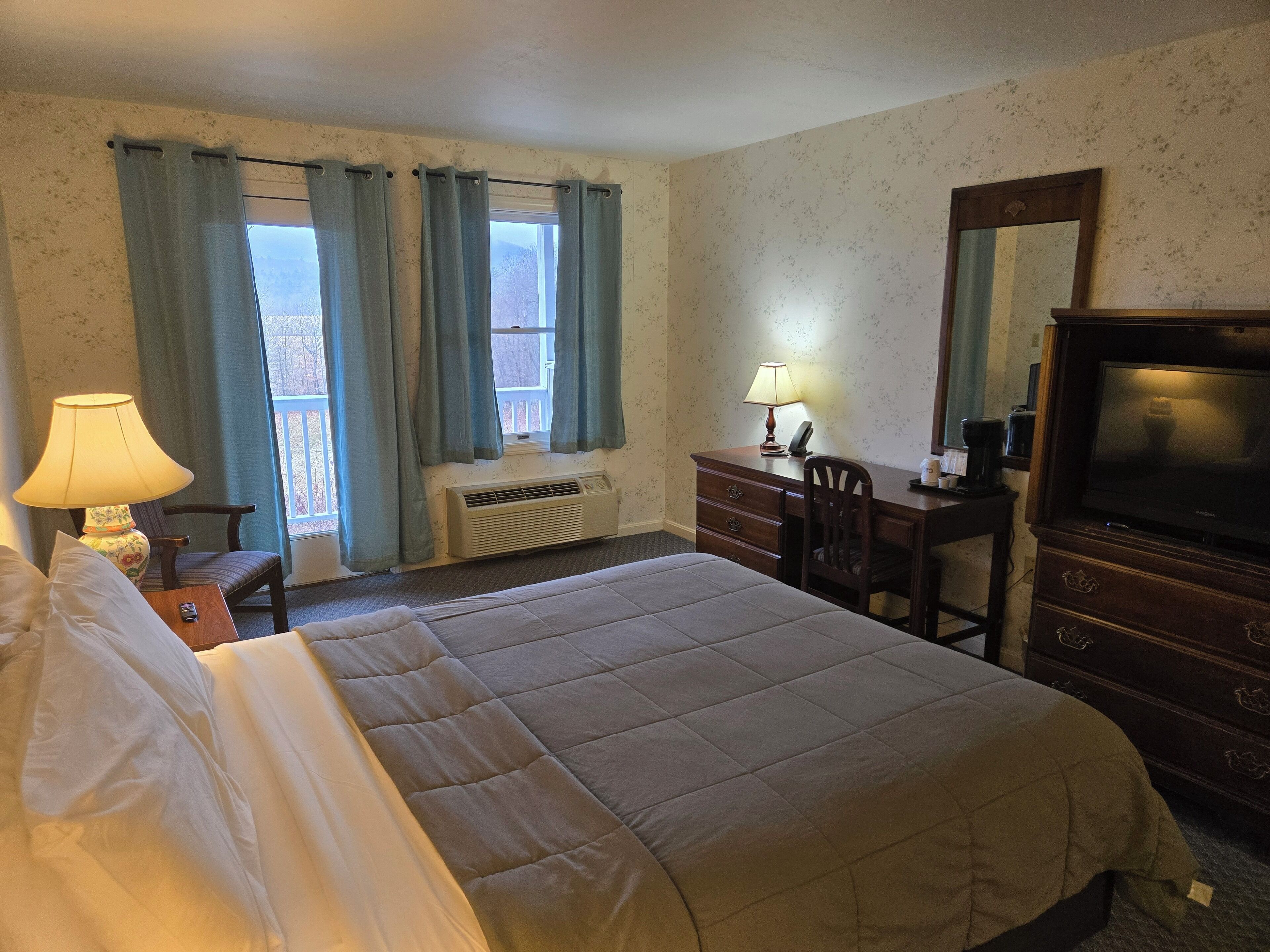 A hotel room with a bed, a desk, a chair, a dresser, a television, and a window with curtains.