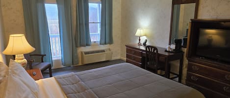 A hotel room with a bed, a desk, a chair, a dresser, a television, and a window with curtains.