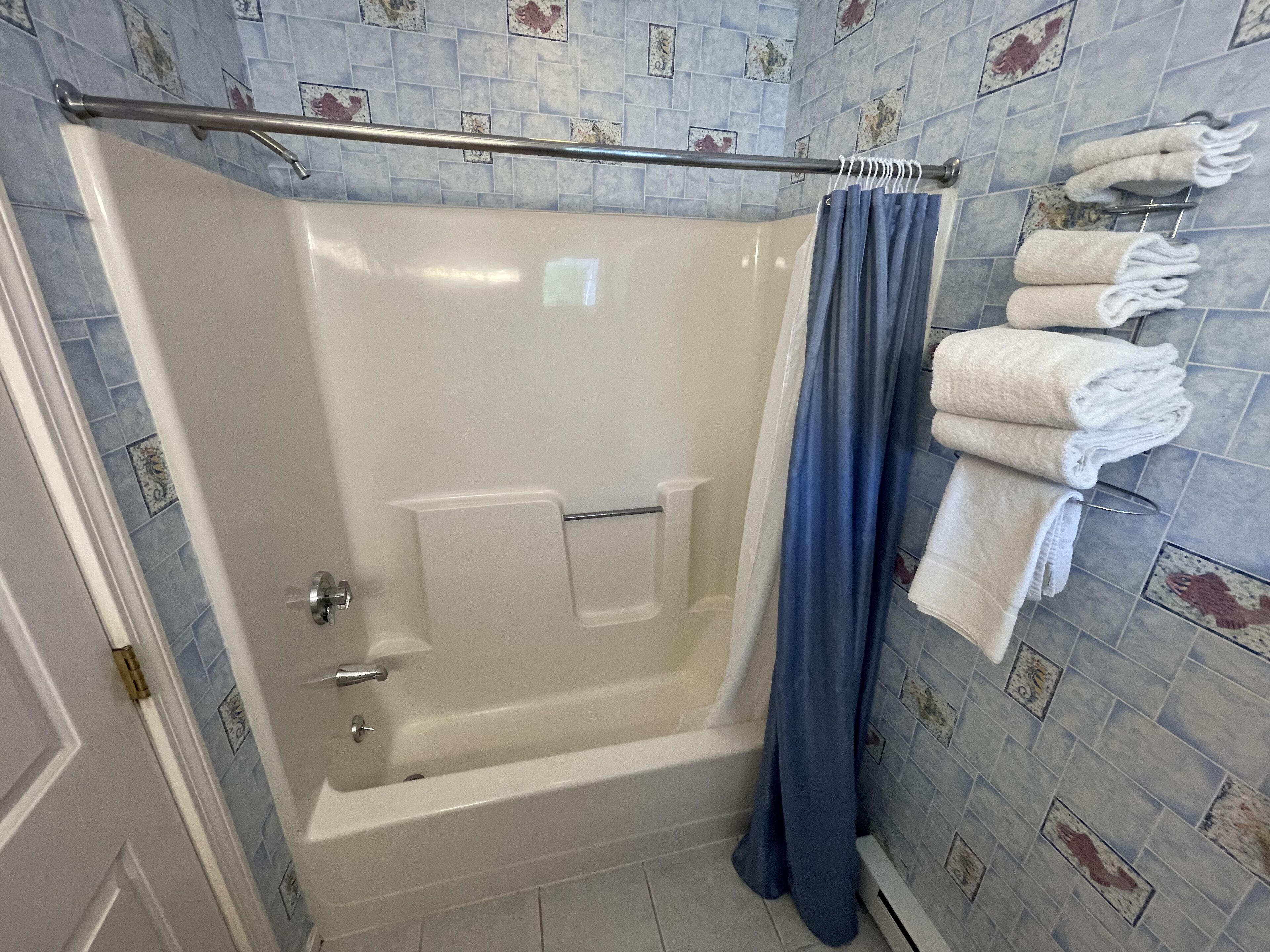 A bathroom with a bathtub, a shower curtain, and a towel rack with towels.