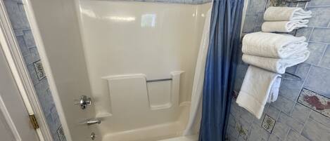 A bathroom with a bathtub, a shower curtain, and a towel rack with towels.