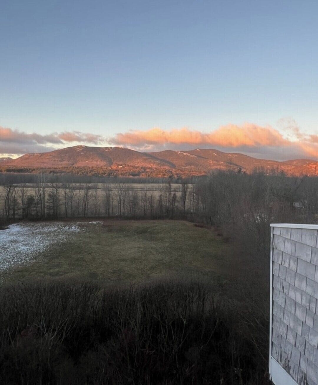 A view of a mountainous landscape with a wooden fence and a building in the foreground.