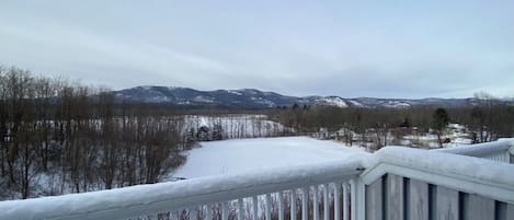 Schneebedeckte Landschaft mit einer Holzdielen-Terrasse und Blick auf ferne Berge.