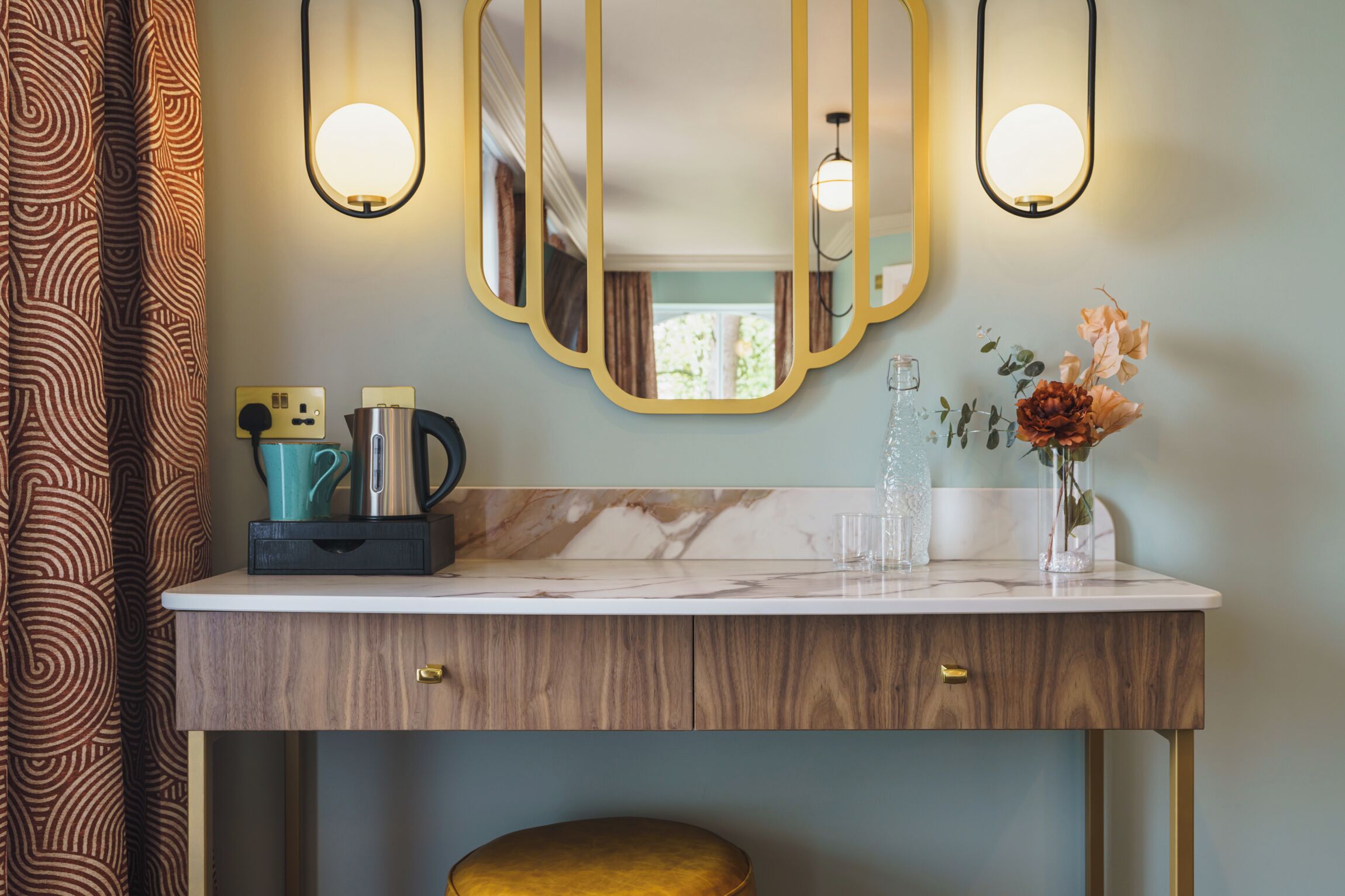 A bathroom with a wooden vanity, a mirror with a gold frame, and a vase with flowers.