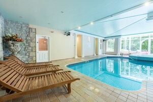 Zona de piscina con tumbonas de madera, un muro de piedra y una puerta que da a una habitación.