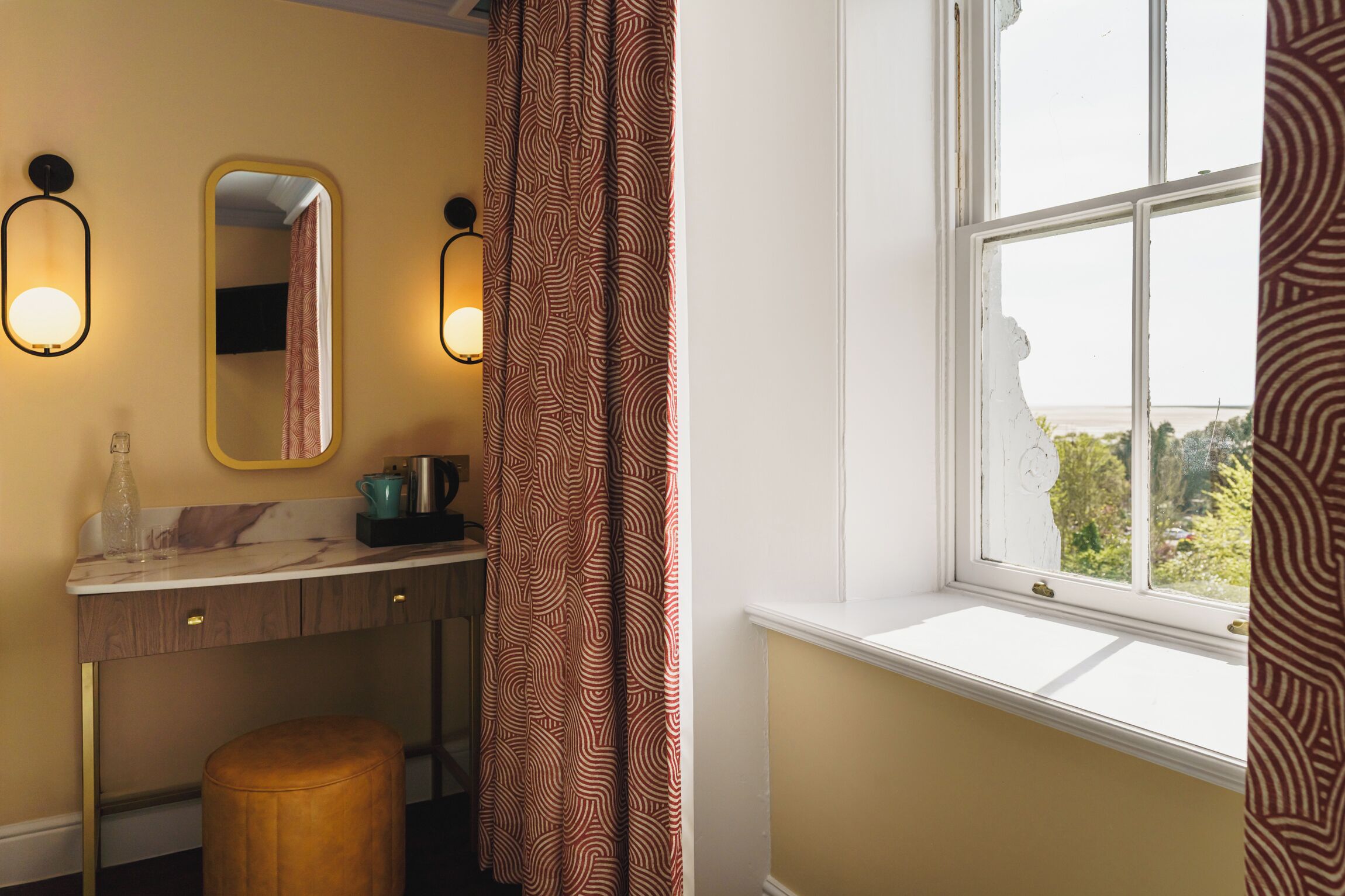 Un baño con tocador, espejo, lavabo, toalla y ventana con vistas.
