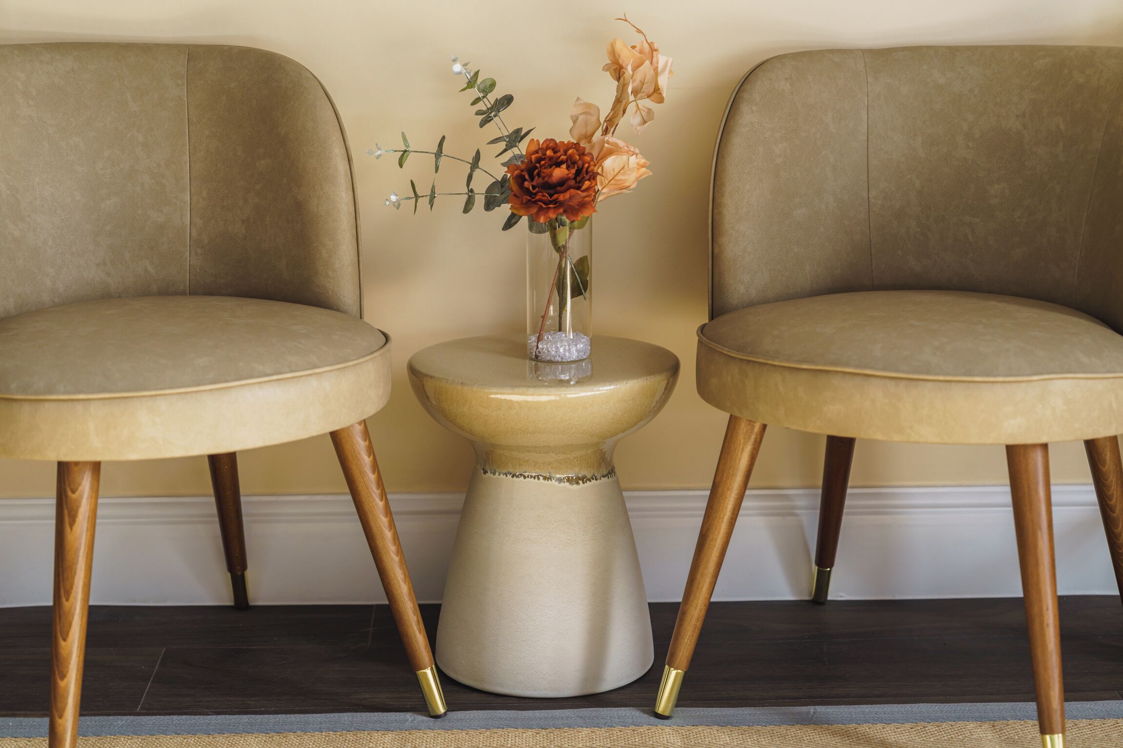 Dos sillas color beige con patas de madera y una mesita baja con un jarrón de flores encima.