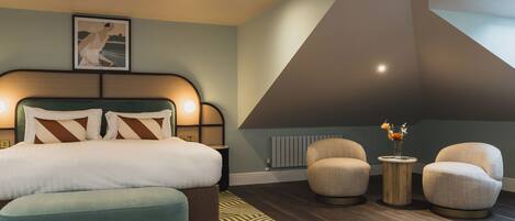 A modern bedroom with a bed, two armchairs, a side table, and a floor lamp.