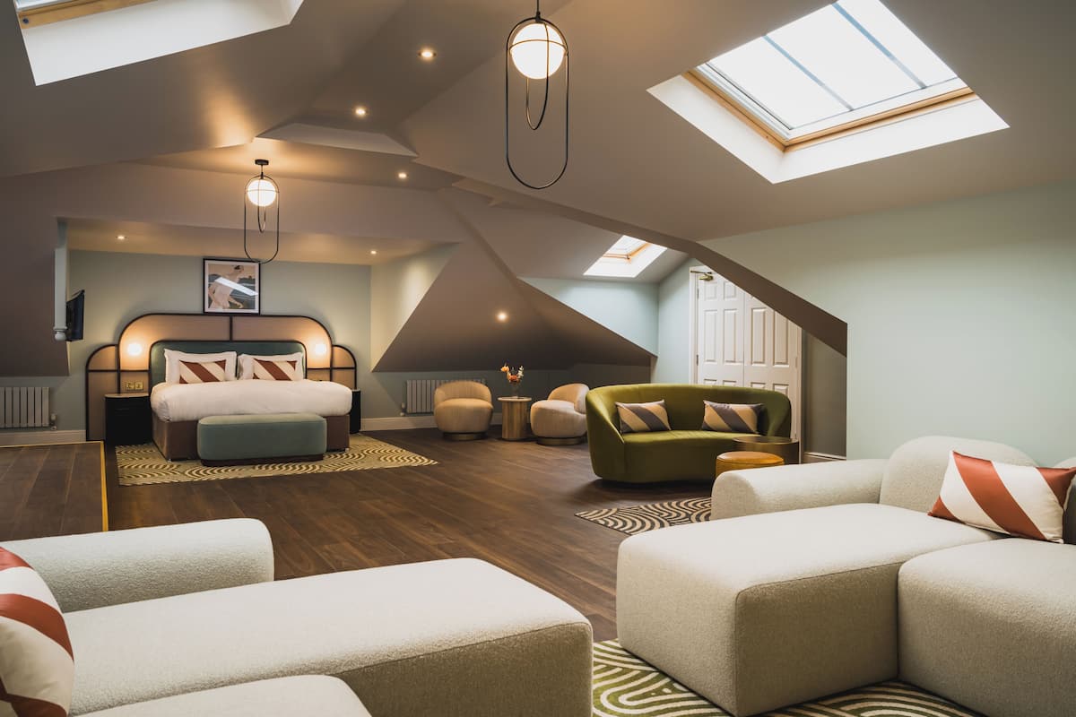 Amplo quarto no estilo loft, com cama grande, área de estar e claraboias.