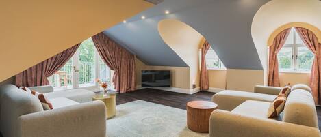 A spacious living room with a high ceiling, a flat-screen TV, and a large window with curtains.