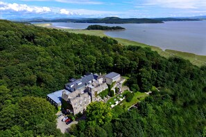 An aerial view of a large estate with a main building surrounded by dense forest, a lake, and a small island. - Grange Hotel (Grange-over-Sands)
