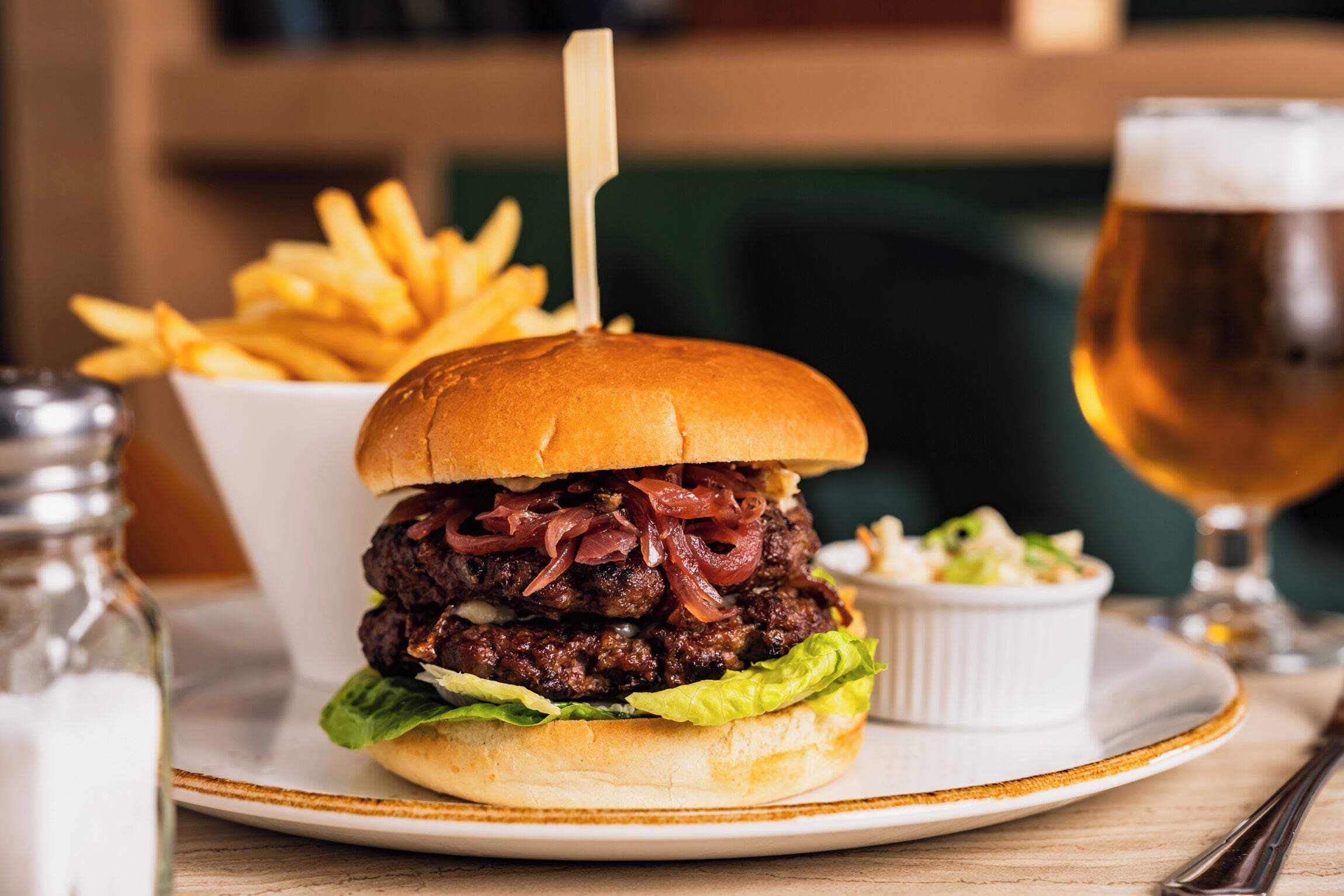 A burger with fries and a glass of beer on a plate.