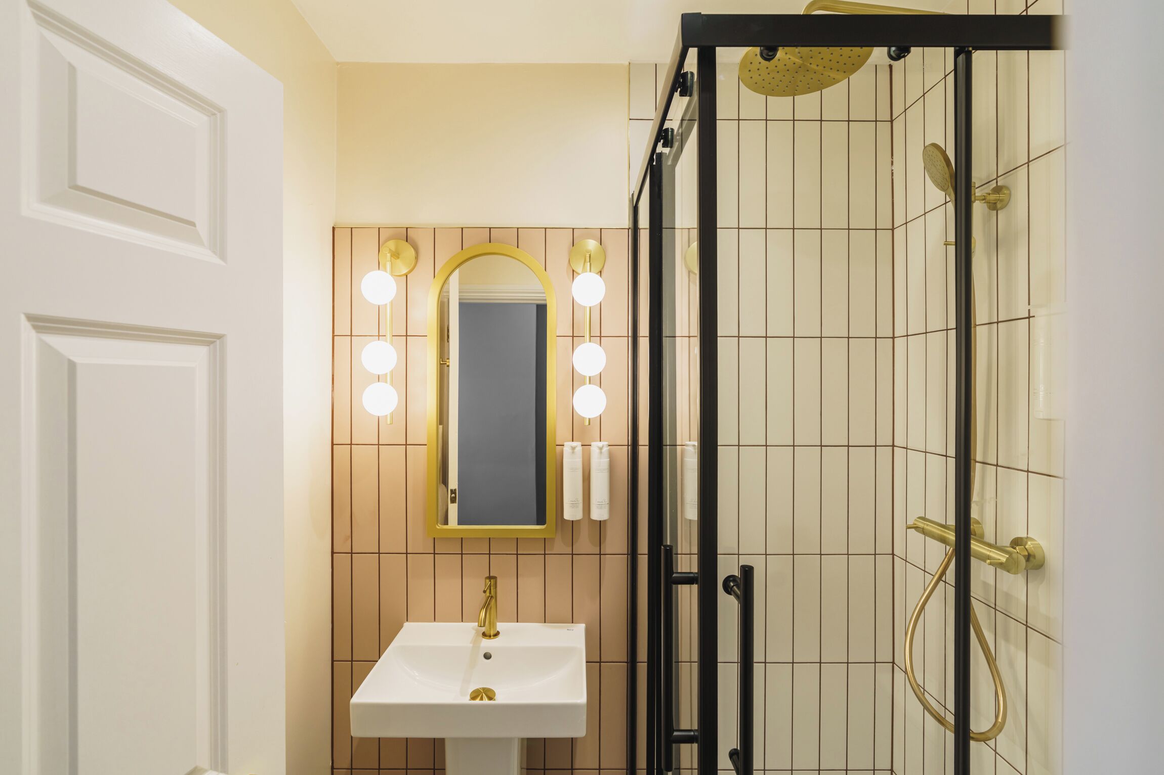 Un baño con lavamanos blanco, detalles dorados y un espejo con luces.
