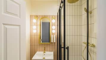 Un baño con lavamanos blanco, detalles dorados y un espejo con luces.