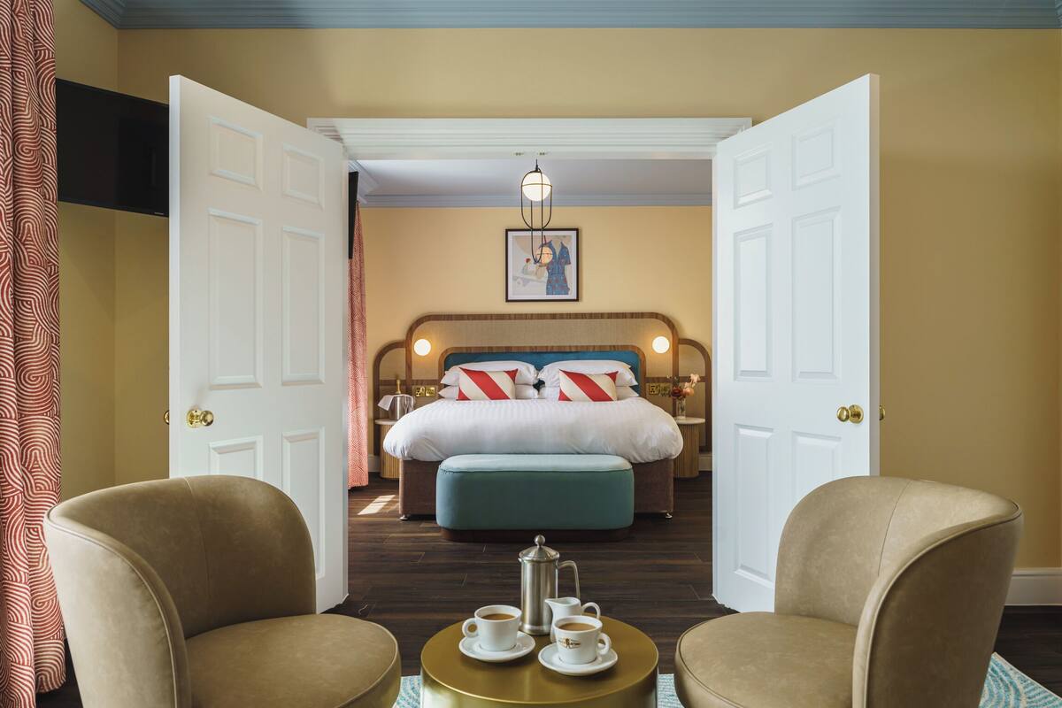 Quarto de hotel com cama, duas poltronas, mesa de centro e um quadro na parede.