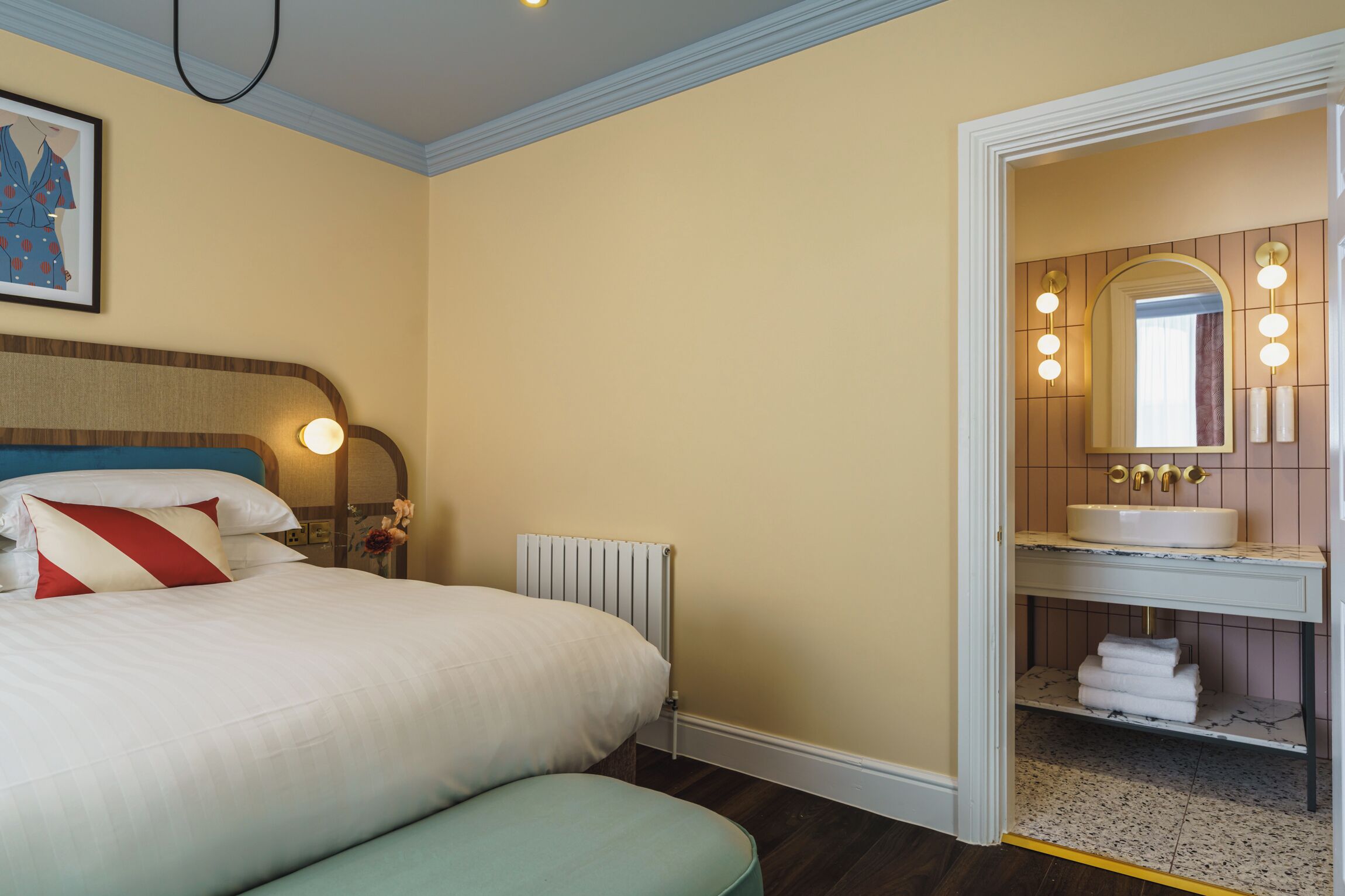 Una habitación de hotel con cama, mesita de noche y baño con lavamanos y espejo.