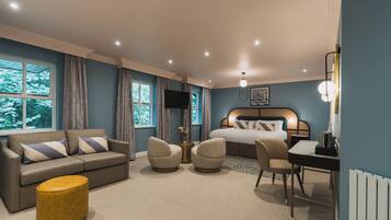 Una habitación de hotel moderna con sofá, sillones, mesa de comedor, cama y televisor.